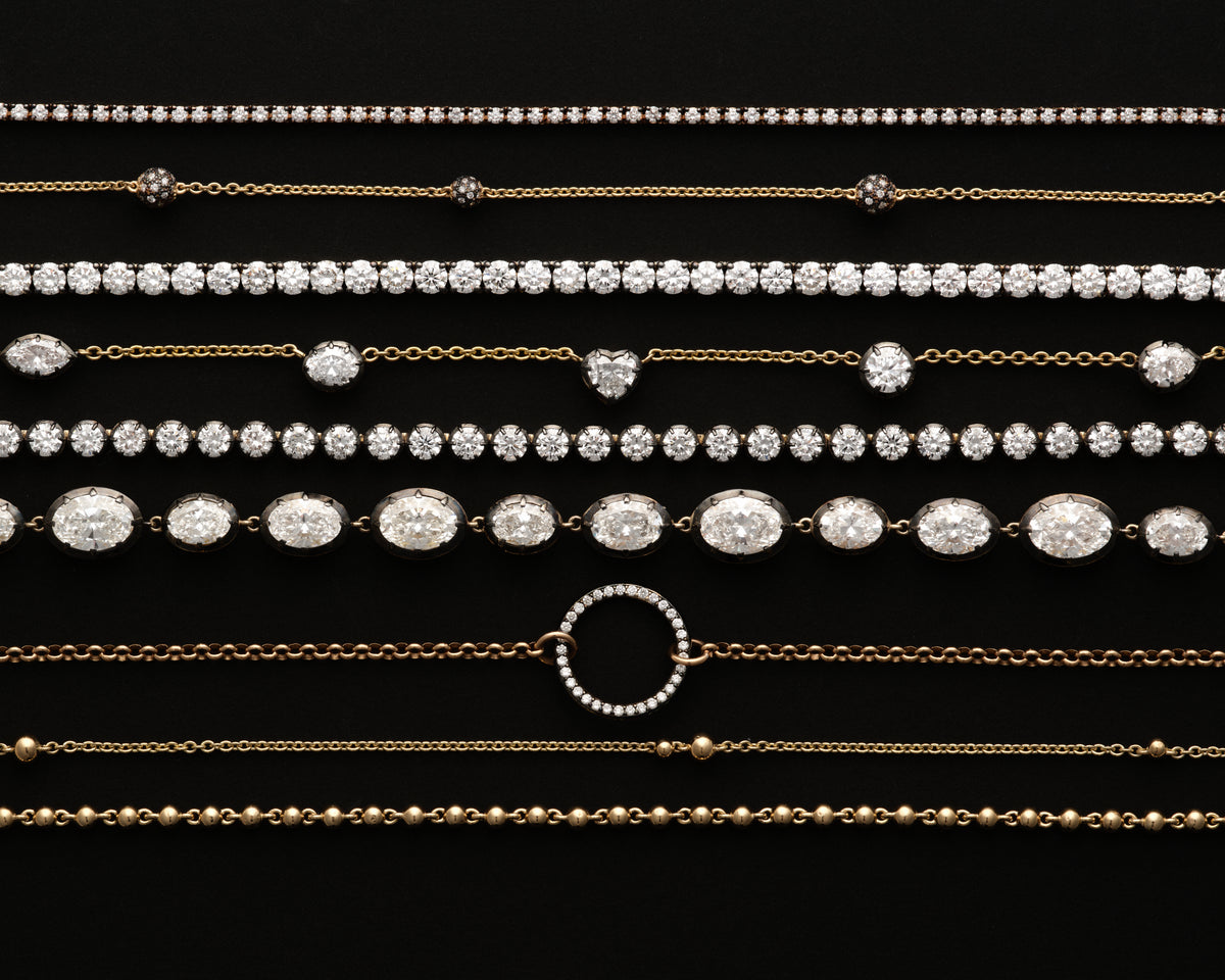 Lab-grown diamond tennis necklaces and gold chains laid out on black